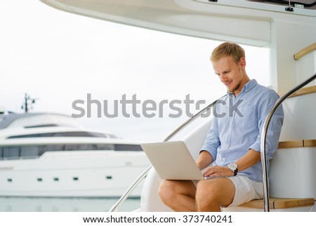 Luxury traveling and working. Handsome young man using laptop on the deck of modern yacht.