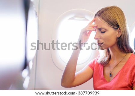 Fear of flying woman in plane airsick with stress headache and motion sickness or airsickness. Person in airplane with aerophobia scared of flying being afraid while sitting in airplane seat.