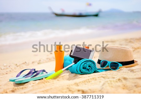 Vacation and technology. Must have accessories on the sea beach. Smartphone, selfie stick, hat, towel and sunglasses.