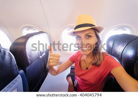 Travel and technology. Young woman in plane taking selfie while sitting in airplane seat.