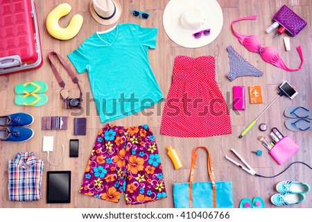 Ready for travel. Overhead of essentials for vacation. Top view of male and female summer accessories, clothes and gadgets on the wooden background. Packing suitcase.