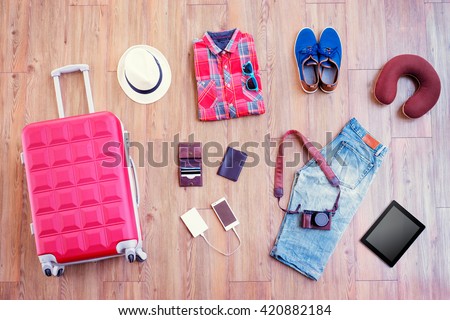 Ready for travel. Essentials for tourist. Top view of male clothes, accessories and gadgets on wooden floor. Valise, wallet, passport, smartphone and powerbank, shoes, camera, hat.