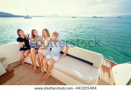 Friendship and vacation. Party on the yacht. Group of laughing young people sitting on the deck drinking champagne sailing the sea.