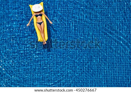 Enjoying suntan. Vacation concept. Top view of slim young woman in bikini on the yellow air mattress in the big swimming pool.