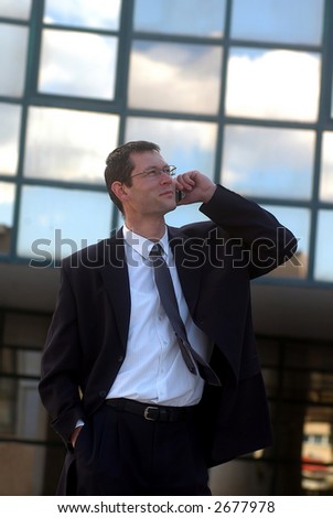 Business call. Young businessman talking to the cell phone in front of an office  .
