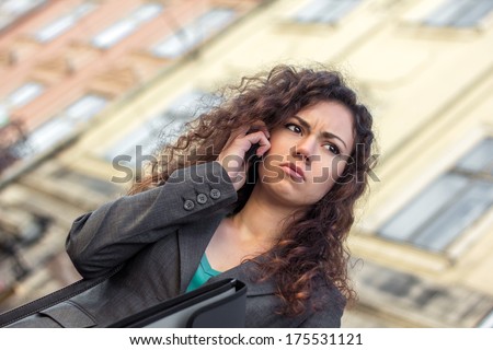 Young upset woman with curly dark hair dressed business style talking on phone outdoor. Sad girl. Business problems. Failure in business. To get upset. To solve the problem. A phone conversation.