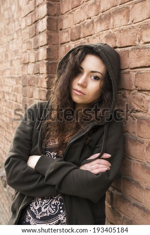 Androgynous girl in hoodie with sad watchful eye on the background of brown wall outdoor