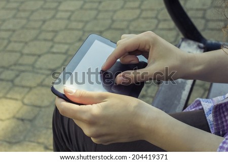 Girl in casual clothes in the park working on a black tablet