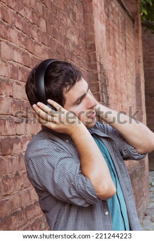 Male music fan in headphones with closed eyes on the street on brick wall background