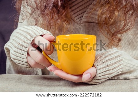 Female hands with orange cup in long sleeves Seater