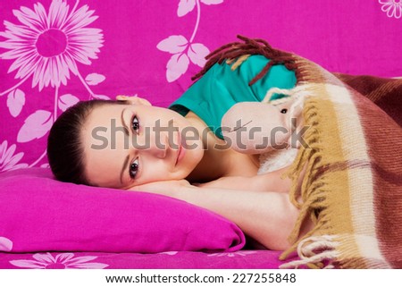 Beautiful brown-eyed brunette girl with open eyes in bed under a blanket with a toy. The girl awakened with a happy smile