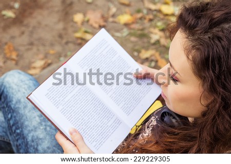 The girl with a book in the park. Young woman with curly hair, resting in an autumn park.