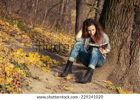 The girl with a book under a tree. Lonely beautiful girl with a book in autumn park.
