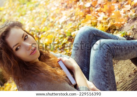Girl with a book in hand in autumn park. Sunny autumn park with fallen leaves. A student with a book on nature.