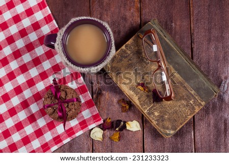 Cup of coffee with milk on the table. Cookies, milk tea and a book on dark table. Cozy mood. Still life on the table of the tablecloth, cup in knitted cover, book and glasses.
