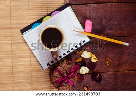 The composition of the notebook, cup of coffee, biscuits and a pencil on the table. A cup of coffee on a notepad. The concept of the new initiatives in business or in life. Snack biscuits.