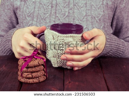Women\'s hands with a cup. Girl drinks coffee from a mug on the kitchen table. Biscuits and coffee or tea for breakfast. Snacking at the table. Cozy home atmosphere.