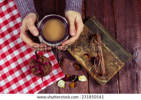Vintage atmosphere. Mug of cappuccino on the table next to the books and biscuits. Embracing a cup of knitted cover. Still life in the kitchen,  the idea of  warm homely atmosphere and cozy mood.