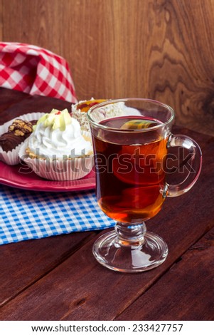 Still life of a glass cup of tea and pastry. Dessert: black tea and sweet cream cakes. Cup of tea on a wooden table with delicious pastries.