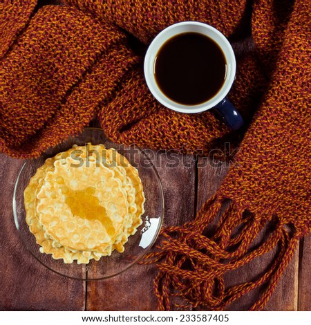 A cup of black coffee next to a honey waffles. Waffles with honey, saucer, cup of coffee and a scarf on the table. Festive atmosphere of warmth and comfort.