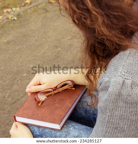 Young girl with book and eyeglasses on a bench in the park. The concept of training, preparation for exams, relaxing in the park.