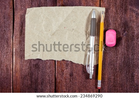 A piece of kraft paper with a pen and pencil on the table. Wooden table with a piece of crumpled brown paper. Office supplies on the table. Theme students and hobby.
