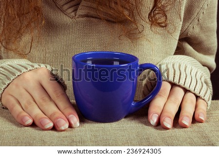 Hands of young woman with a cup of tea. Girl in sweater with long sleeve with a cup of tea.