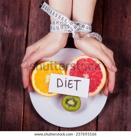The concept of eating disorders: bulimia, anorexia, diet fads. Women's hands tied centimeter. Girl's hands with a plate and fruit. Fruit diet. Low-fat diet.