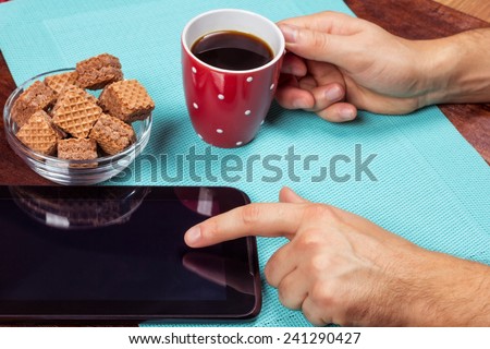Office desk with a tablet, a cup of black coffee and male hands. The man with the tablet. Life office worker. Waffles, black coffee and a computer.