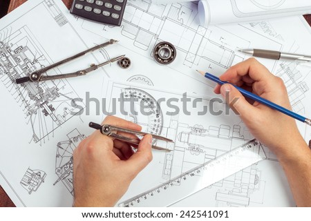 Man's hand with a compass. Mechanical engineer at work. Technical drawings. Pencil, compass, calculator and hand man. Paper with technical drawings and diagrams.