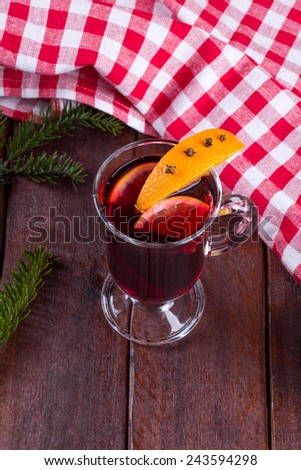 A glass of mulled wine on the table. Mulled wine with citrus slices on a table next to a Christmas tree branch and tablecloths. The atmosphere of celebration and fun.
