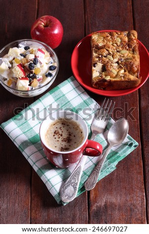 A bowl of fruit salad, apple pie and cappuccino on the table. Hearty and healthy breakfast or lunch. Baking, apples and yogurt, coffee. Vintage atmosphere