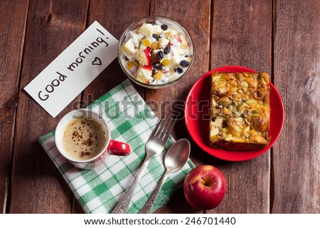 Apple pie, fruit salad and a cup of cappuccino on the table. Surprise with a wish good morning. Homemade pie with seeds, a cup of coffee and diet fruit salad with yogurt on the table.