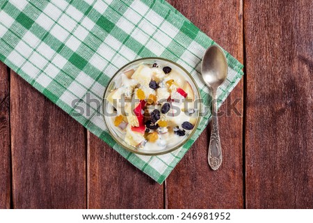 Fruit salad on a napkin, top view. A bowl of salad with apples, raisins and yogurt on the table. Spoon, bowl and towel on the table. Kitchen table. Breakfast for weight loss.