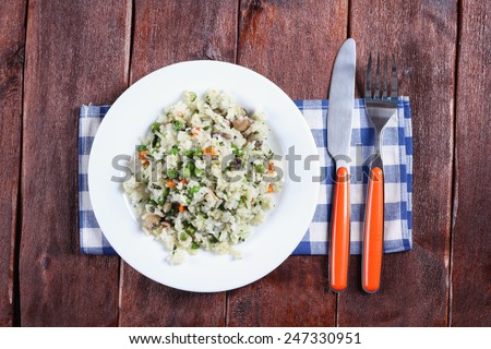 Risotto dish with cutlery on the table. Wooden table, napkin, plate of rice with vegetables and cutlery. Italian cuisine. Plate with rice for lunch.