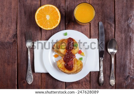 Simple and nutritious breakfast: toast, fried in egg and milk. Jam, candied fruits, glass of juice, orange and cutlery on the table.