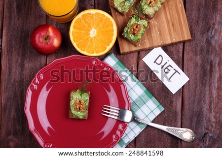 Healthy diet food. Canape with avocado paste, herbs and nuts. Delicious breakfast: orange juice, canapes and half an orange. Plate, glass, cutting board and banner with  inscription.