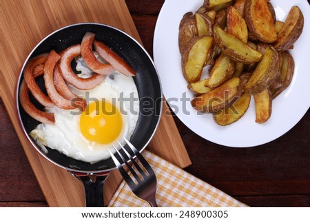 Frying pan with fried egg and sausages near the plate with baked potatoes. Top view. Classic hearty lunch. German cuisine. International cuisine. Calorie fried food.