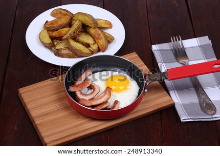 Frying pan with fried eggs and sausages near the plate with baked potatoes. Classic hearty lunch. German cuisine. International cuisine. Calorie fried food.