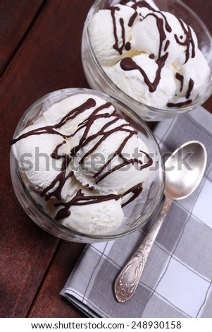 Sweet dessert. Two servings of vanilla ice cream with chocolate icing. Bowls of ice cream, spoon and napkin. Ice cream on the kitchen table. Serving dishes in the cafeteria or restaurant.