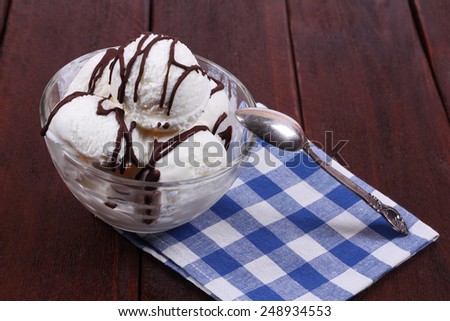 Vanilla ice cream with chocolate icing. Bowls of ice cream, spoon and napkin. Ice cream on the kitchen table. Serving dishes in the cafeteria or restaurant.