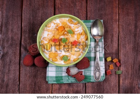 A bowl of cornflakes with milk and candied fruits near lychee. Lychee, cereal bowl and spoon on the table. Top view. Easy and nutritious breakfast. Quick breakfast.
