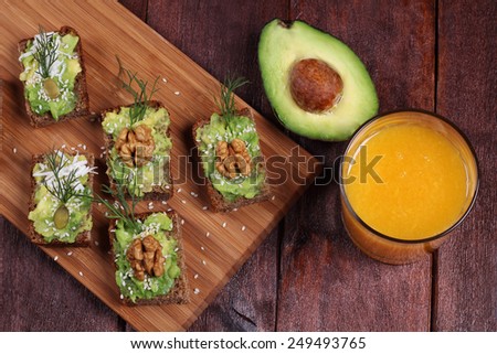 Canape with avocado, walnuts, sunflower seeds, cheese and dill. Half an avocado, snacks and a glass of orange juice. Top view. Nutritious and healthy lunch.