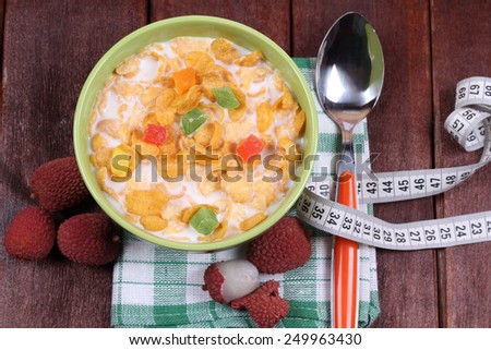 Green bowl with milk and corn flakes. A bowl of cereal, candied fruit and milk on the table. Bowl, spoon, measuring tape and lychee. Chinese plum. Diet food. Quick breakfast.