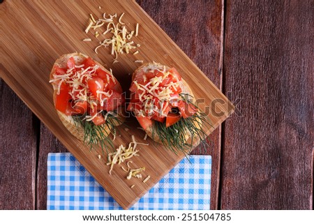 Bruschetta with tomato and grated cheese on the board. Cutting board with a snack - bruschetta with tomato. Delicious and easy appetizer.