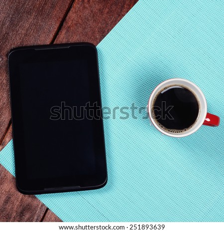 Tablet computer and a cup of strong coffee on the table. Top view. The handheld PDA and a mug of coffee. The concept of business and start up.