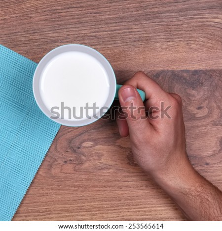 Man\'s hand with a cup of cow\'s milk. A man holding a cup of milk. Turquoise mug with milk on the table. Top view. Studio shoot.