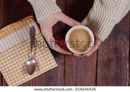 Female hands in a sweater on a long sleeve. Hands and a cup of coffee with milk. Cozy morning. Girl with a cup of latte. Drinking coffee in the kitchen. In search of inspiration. Top view.