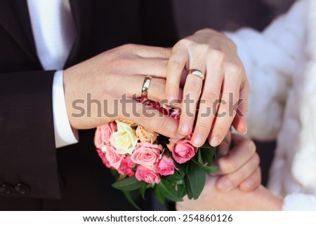 Hands with rings of white gold. Wedding rings. Bride and groom at the wedding. Hands of the bride and groom at a wedding bouquet. Bouquet of roses and hands with rings.