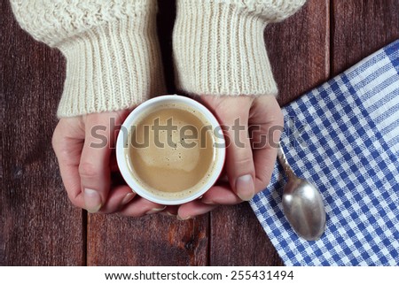 Women\'s hands with a hot cup of coffee. Coffee with milk, latte. A cup of coffee on the table. Embracing a cup of coffee. Cozy home atmosphere. Morning coffee. Toned image.